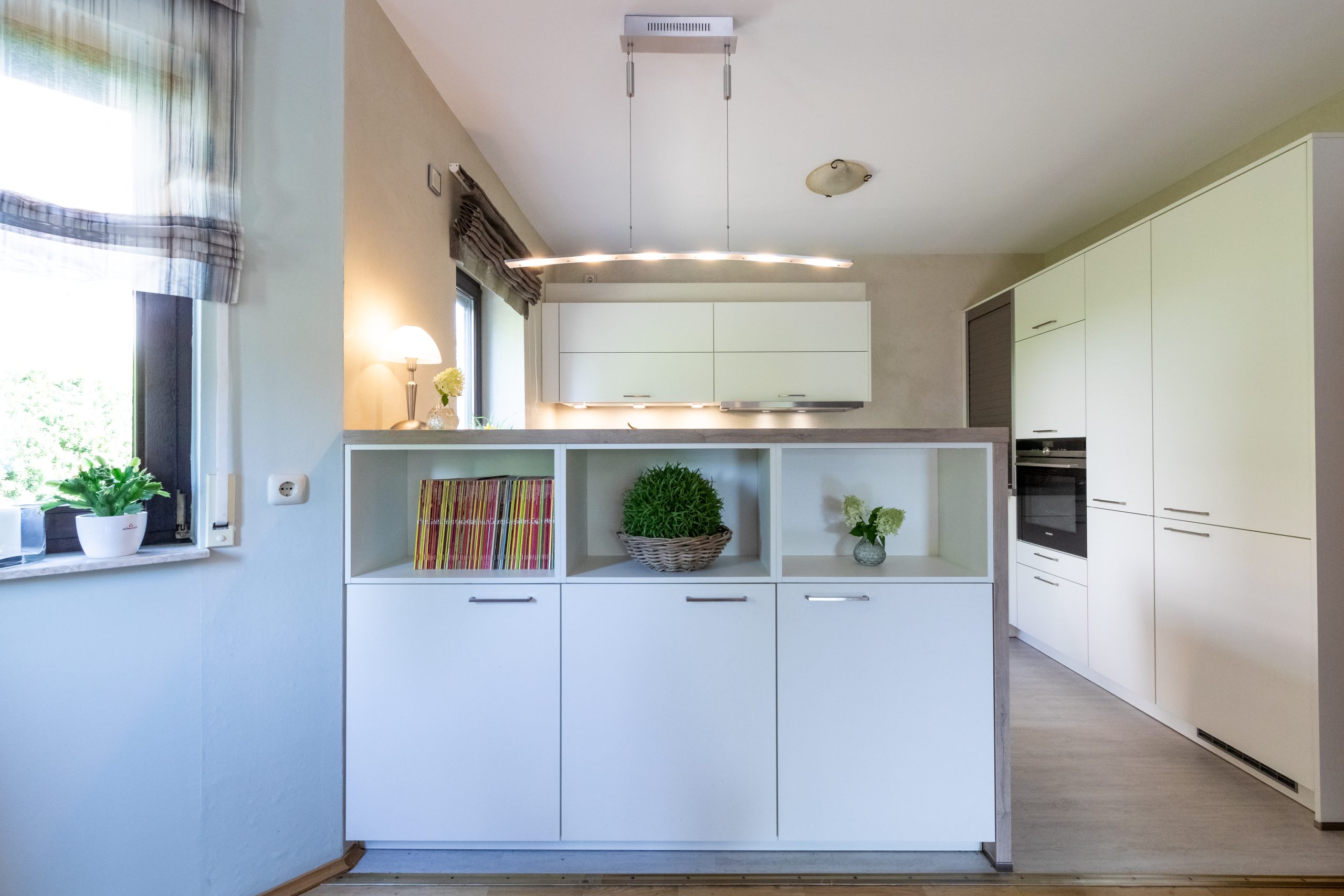 Weiße Küche mit Raumteiler und natürlicher Beleuchtung