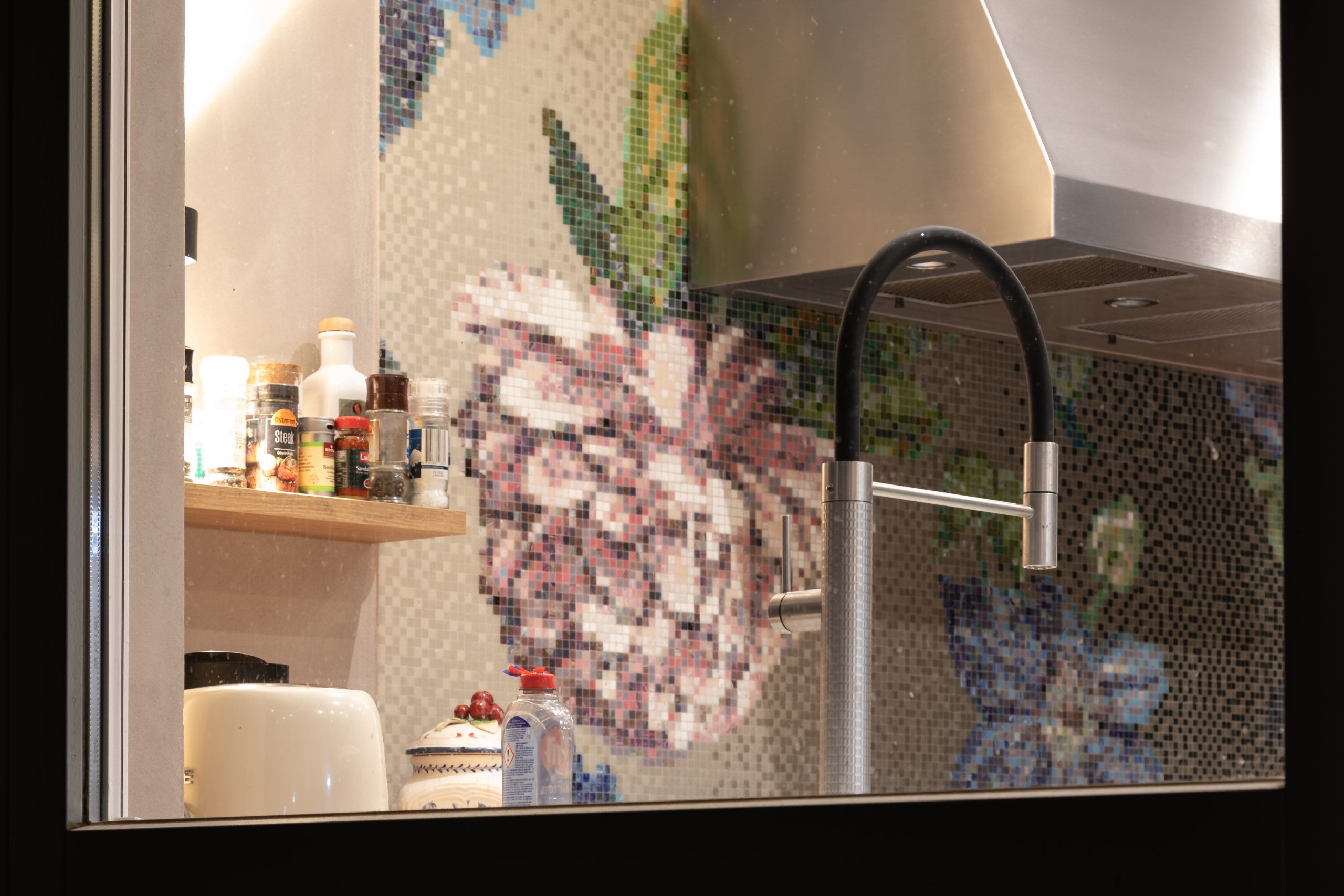 Küchenspüle vor floraler Mosaikfliese mit Gewürzregal im Hintergrund