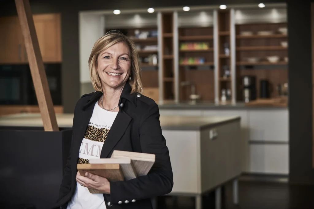 Eine blonde Dame mit schwarzem Sakko schaut selbstbewusst in die Kamera – bereit für eine Beratung. Ein Beispielbild für Küchenplaner Frankfurt.
